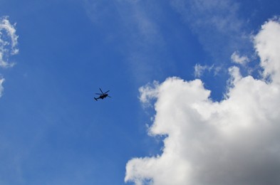 Modern helicopter flying in blue cloudy sky, low angle view