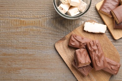 Tasty chocolate bars and nougat on wooden table, flat lay. Space for text