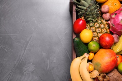 Different tropical fruits in wooden box on grey background, top view. Space for text