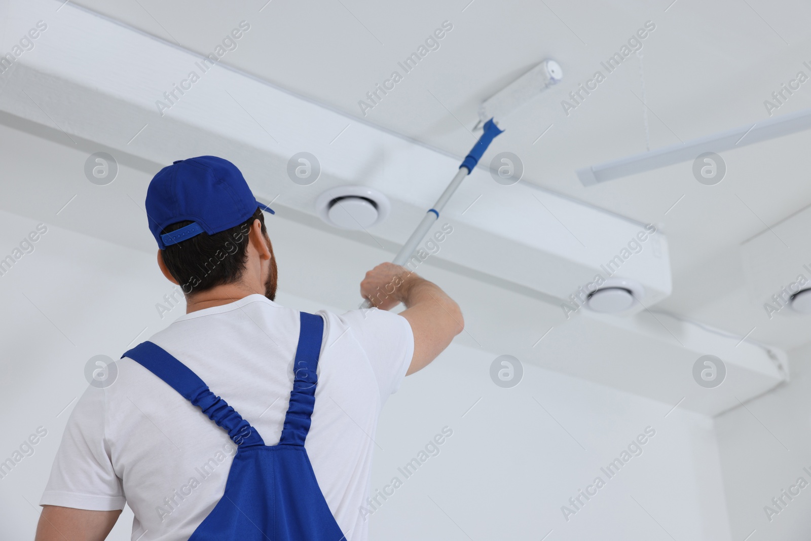 Photo of Handyman painting ceiling with roller in room, back view