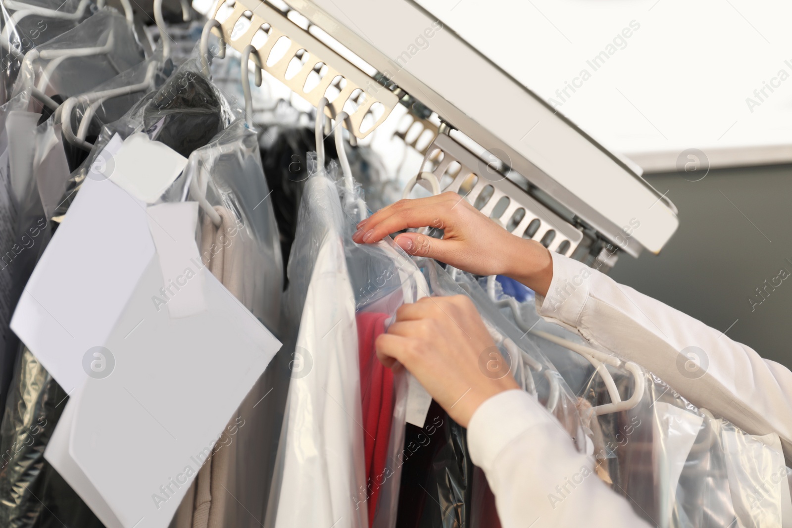 Photo of Female worker taking clothes from garment conveyor at dry-cleaner's, closeup