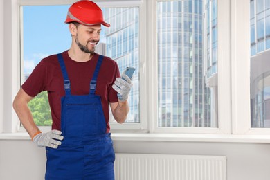 Photo of Professional repairman in uniform with phone indoors, space for text