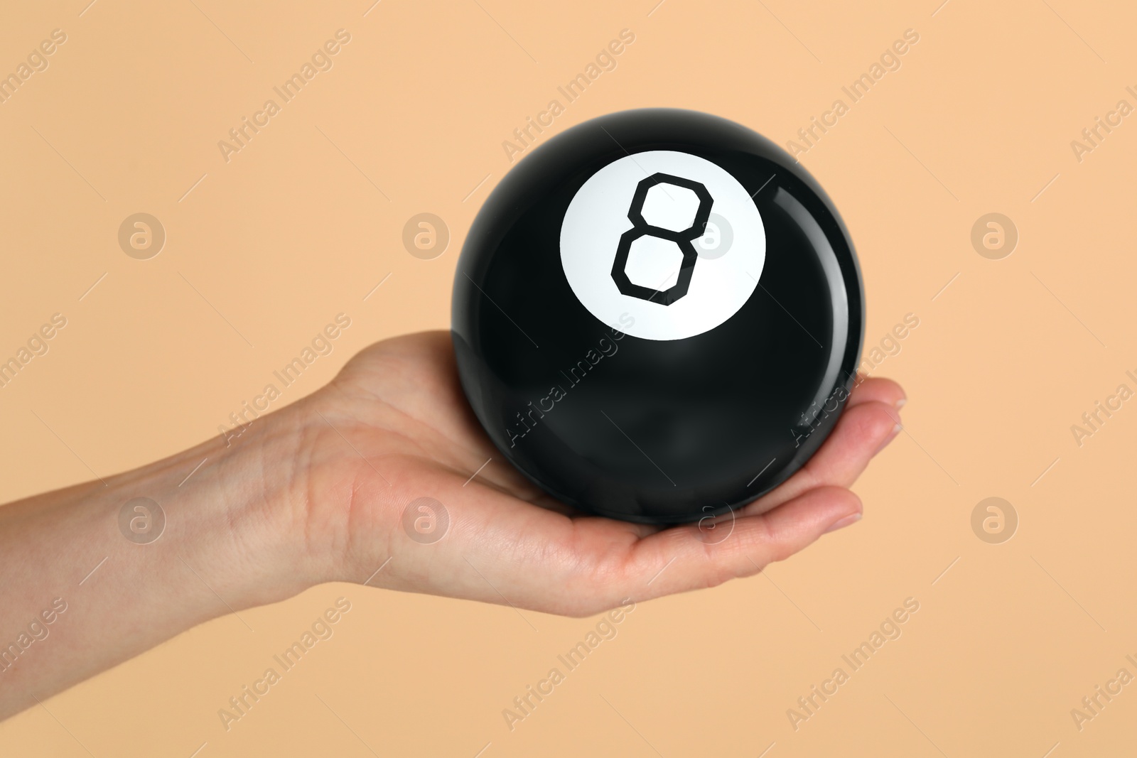 Photo of Woman holding magic eight ball on light brown background, closeup