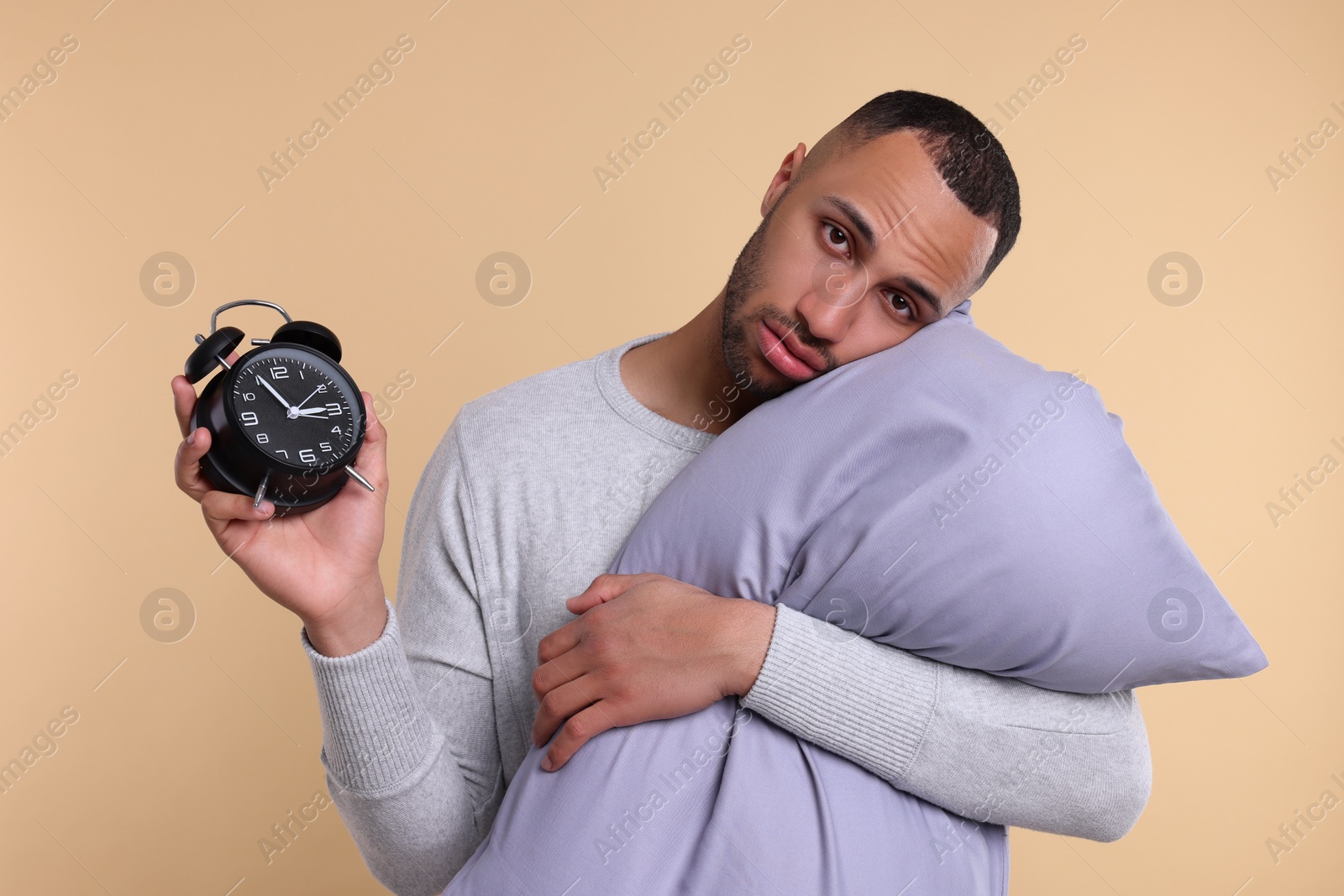 Photo of Sleepy man with pillow and alarm clock on beige background. Insomnia problem