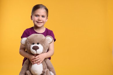 Photo of Cute girl with teddy bear on orange background, space for text