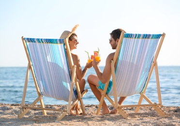 Photo of Young couple with cocktails in beach chairs at seacoast