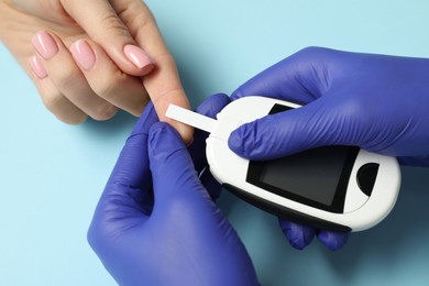 Diabetes. Doctor checking patient's blood sugar level with glucometer on light blue background, top view