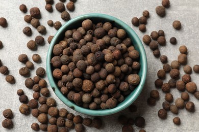 Photo of Aromatic allspice pepper grains and bowl on grey table, top view