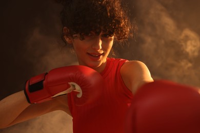 Photo of Beautiful young woman with boxing gloves on color background in neon lights and smoke