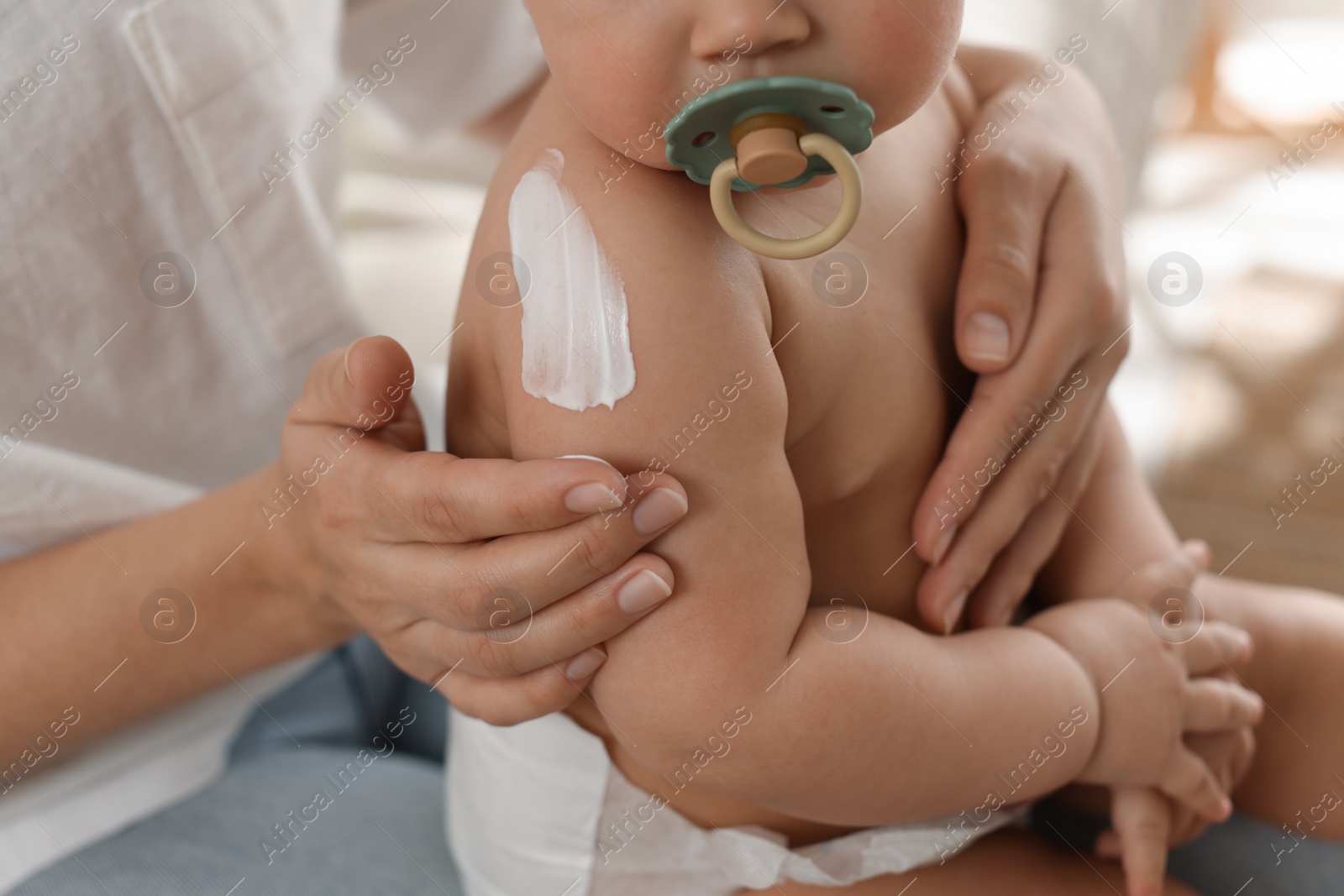 Photo of Mother applying body cream on her little baby at home, closeup