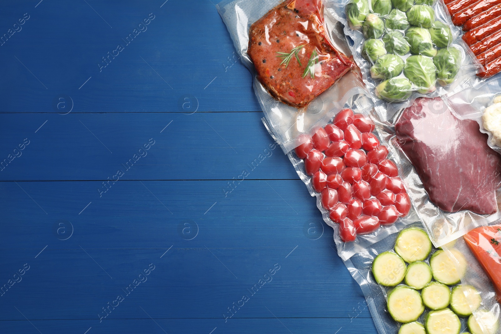 Photo of Flat lay composition of different food in vacuum packings on blue wooden table. Space for text