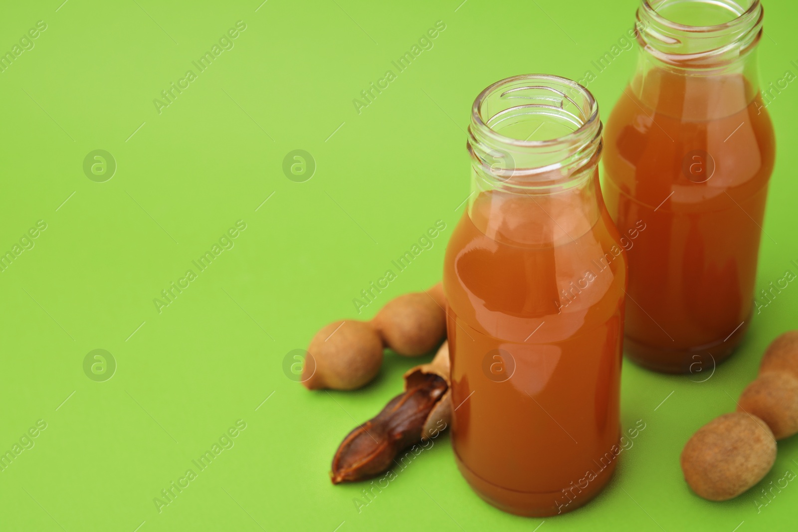 Photo of Tamarind juice and fresh fruits on green background, space for text