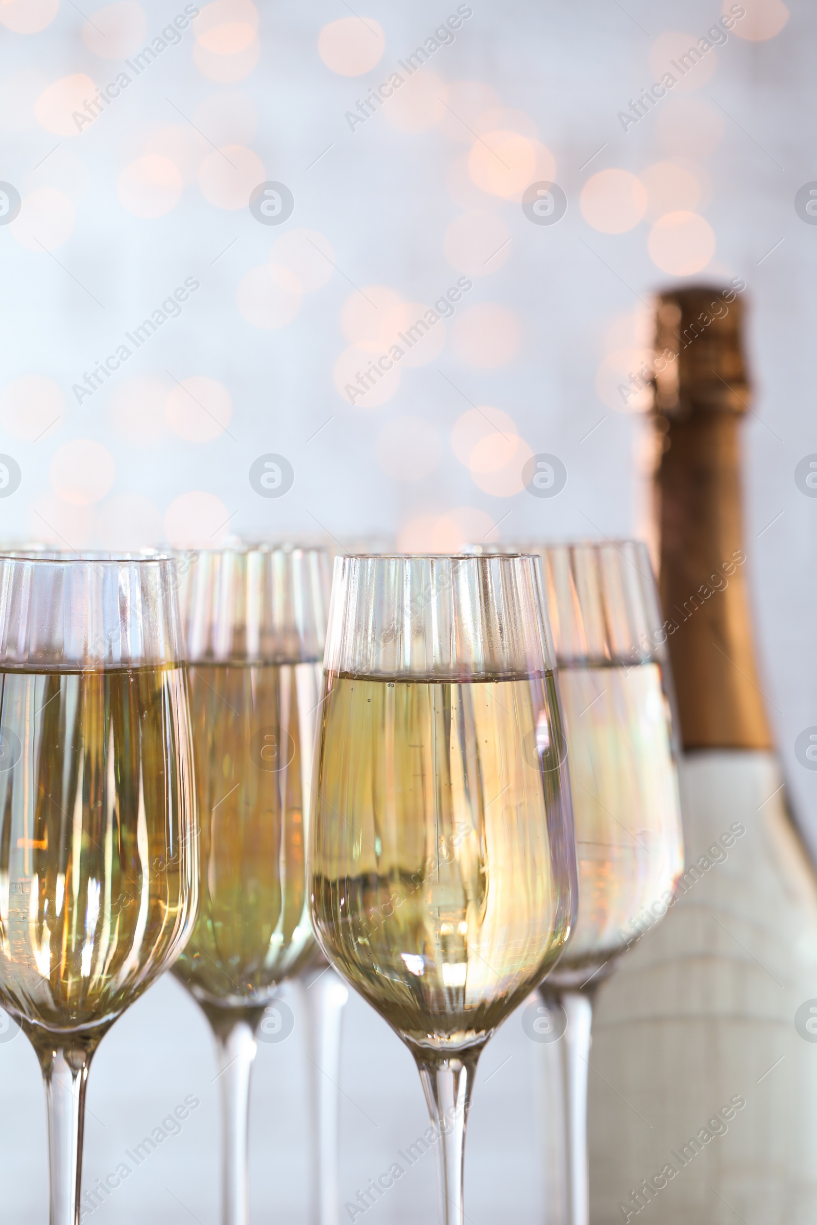 Photo of Glasses of champagne and bottle against blurred lights, closeup