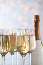 Photo of Glasses of champagne and bottle against blurred lights, closeup