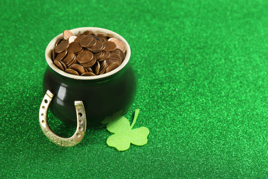 Photo of Pot of gold coins, horseshoe and clover on green background, space for text. St. Patrick's Day celebration