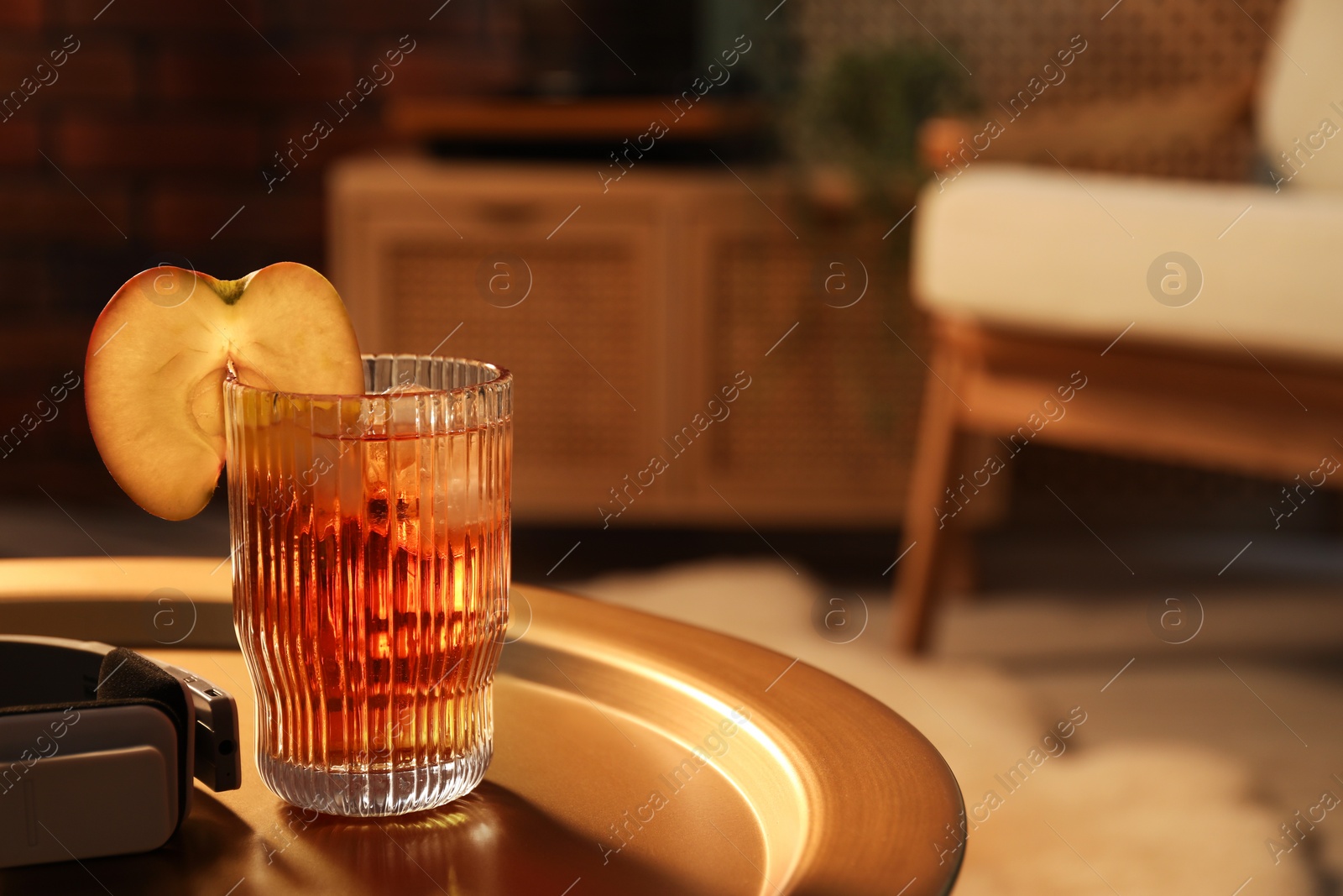 Photo of Glass of tasty cider and headphones on table in room, space for text. Relax at home