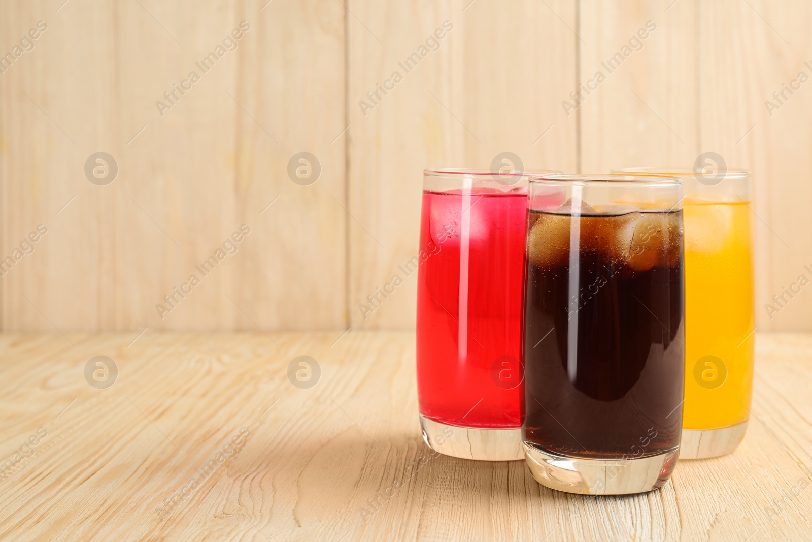 Photo of Glasses of different refreshing soda water with ice cubes on wooden table. Space for text