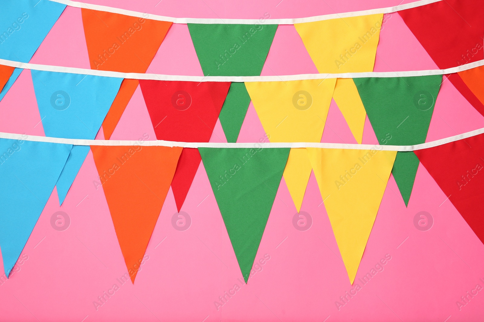 Photo of Buntings with colorful triangular flags on pink background. Festive decor