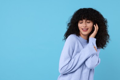 Happy young woman in stylish warm sweater on light blue background, space for text