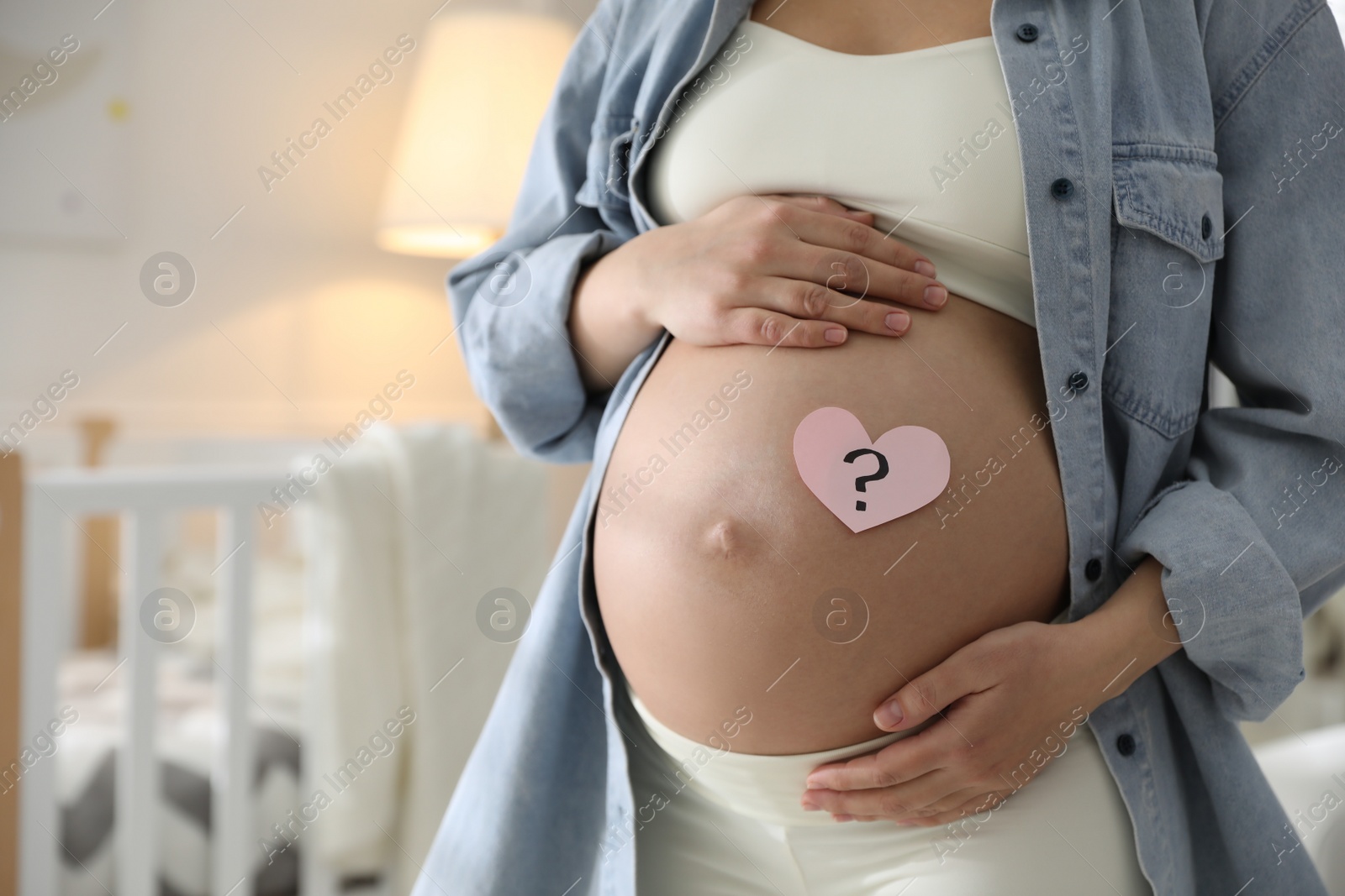 Photo of Pregnant woman with heart shaped sticky note on belly indoors, closeup. Choosing baby name