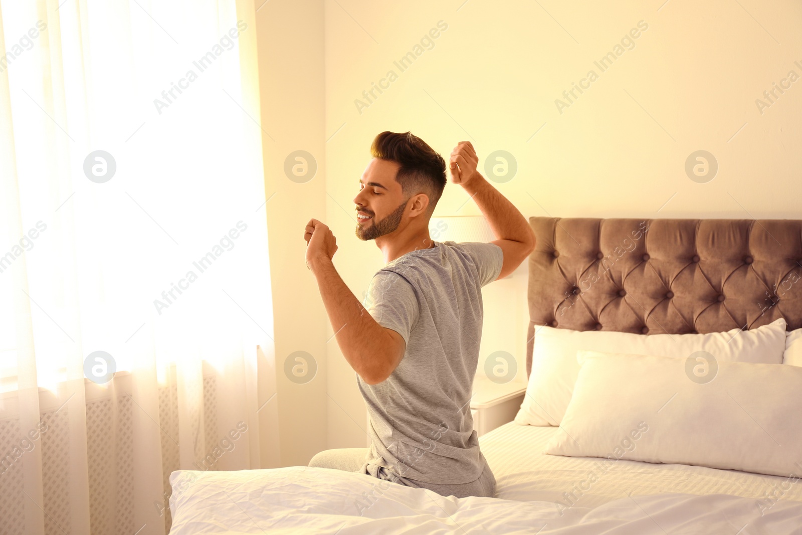 Photo of Young man stretching on bed at home. Lazy morning