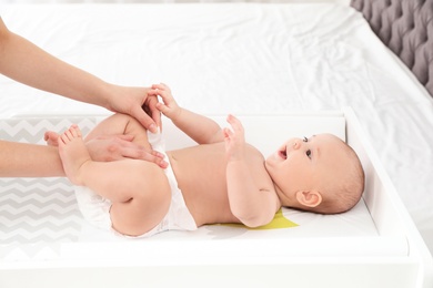 Mother changing her baby's diaper on table indoors