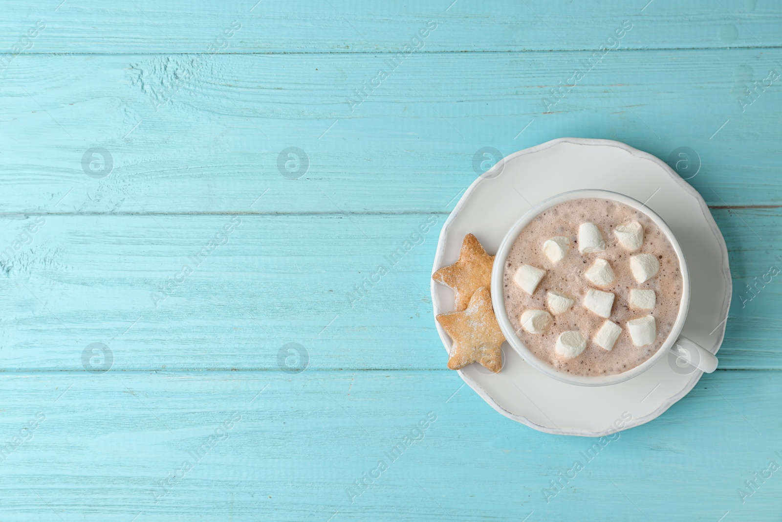 Photo of Delicious hot cocoa drink with marshmallows in cup and cookies on light blue wooden background, top view. Space for text
