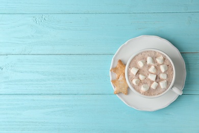 Photo of Delicious hot cocoa drink with marshmallows in cup and cookies on light blue wooden background, top view. Space for text