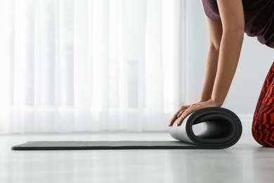 Young woman rolling yoga mat indoors, closeup. Space for text