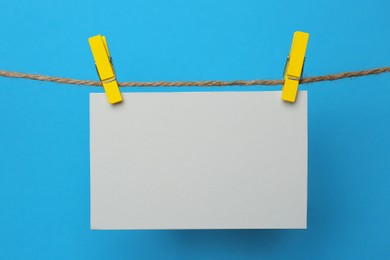 Photo of Wooden clothespins with blank notepaper on twine against light blue background. Space for text