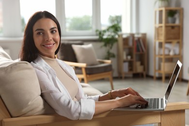 Photo of Young woman working with laptop on sofa at home