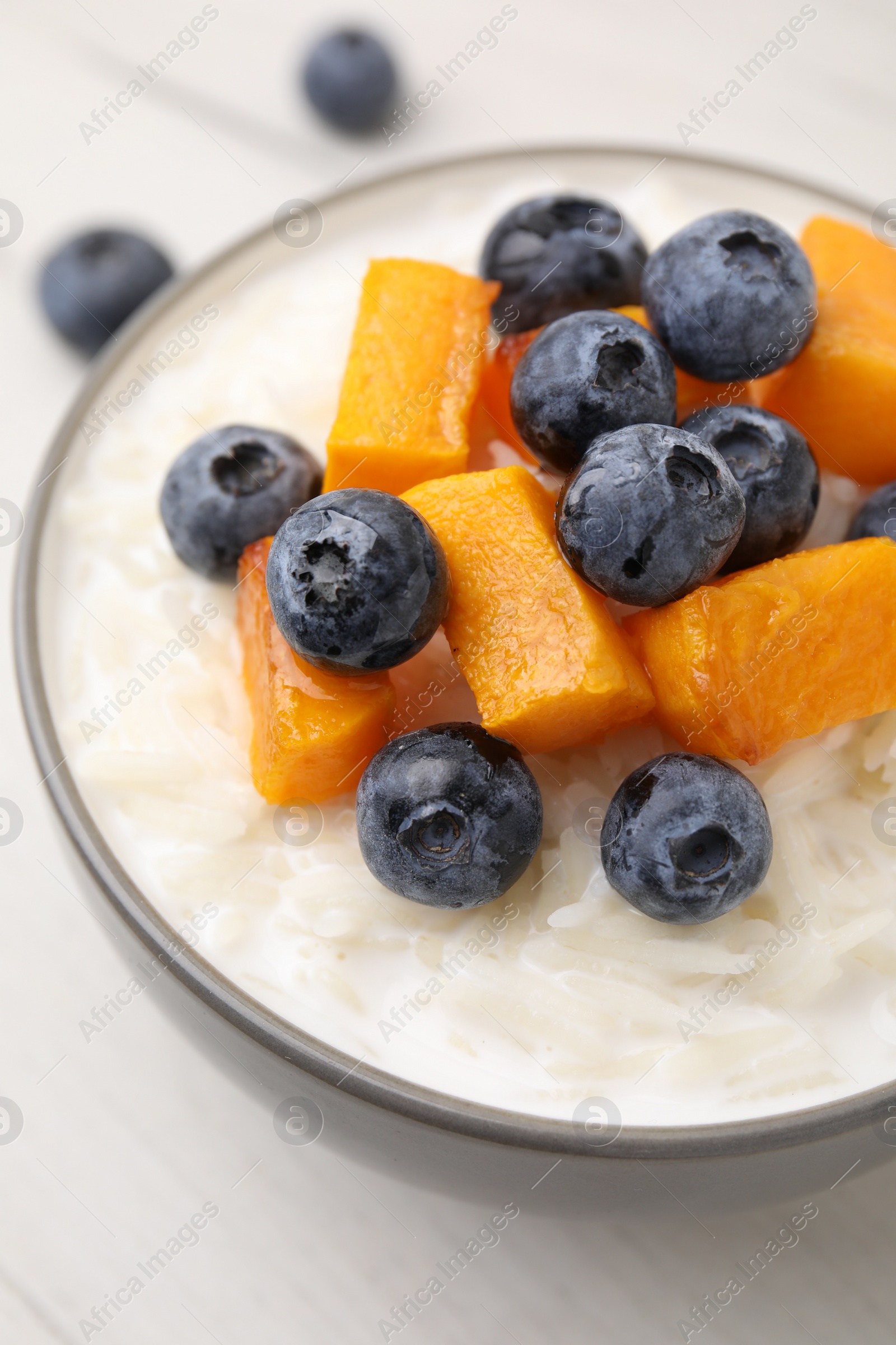 Photo of Bowl of delicious rice porridge with blueberries and pumpkin on table, closeup