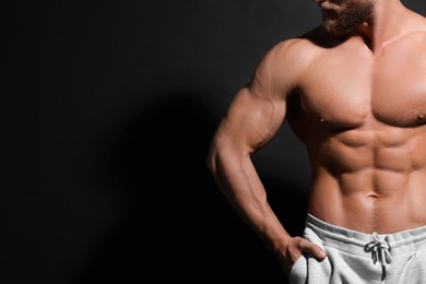 Photo of Muscular man showing abs on black background, closeup and space for text. Sexy body