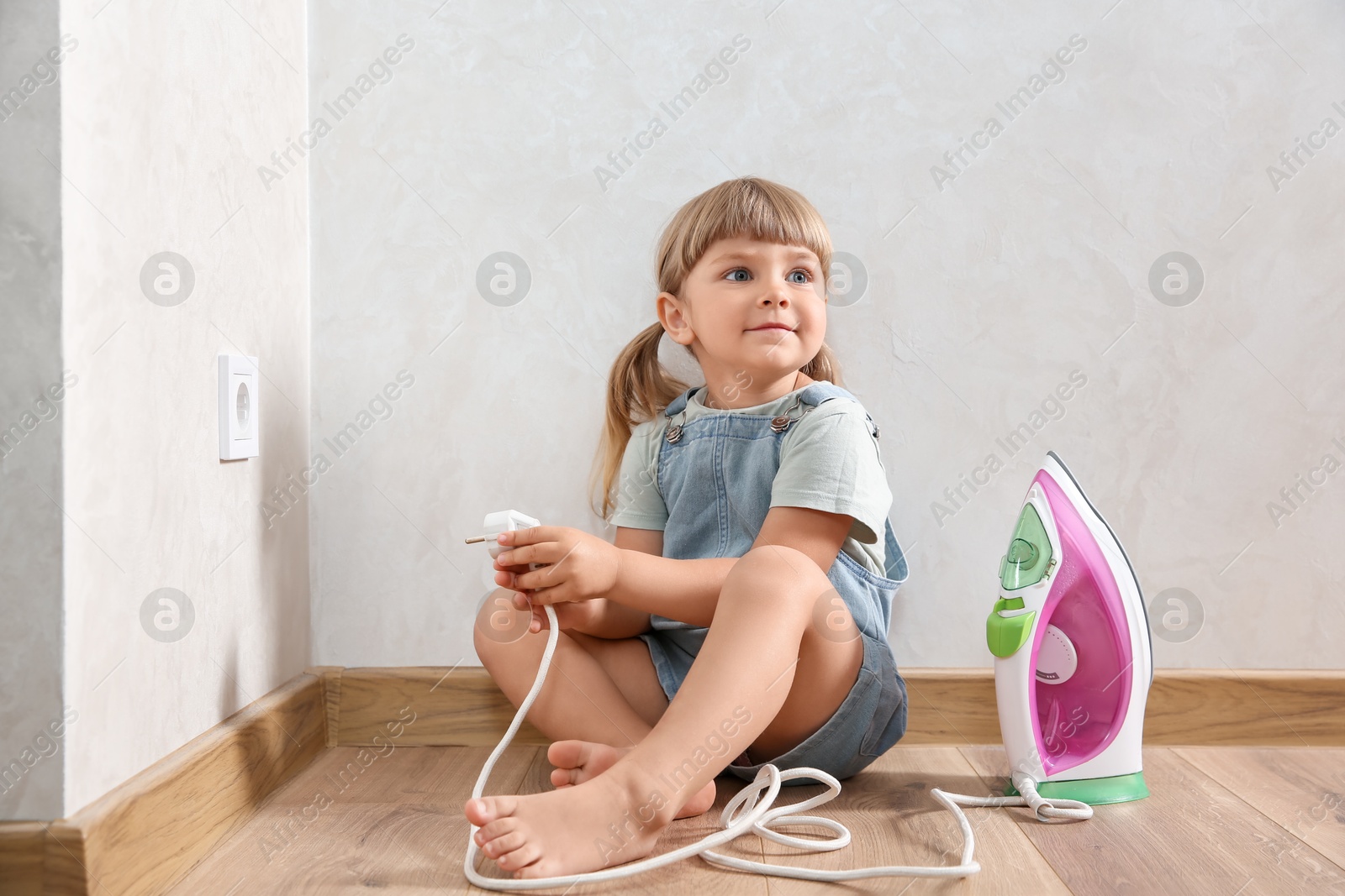 Photo of Little child playing with iron plug near electrical socket at home. Dangerous situation