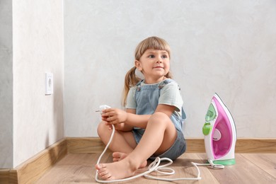 Little child playing with iron plug near electrical socket at home. Dangerous situation