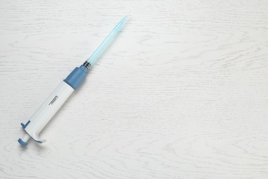 Photo of Laboratory analysis. Micropipette with liquid on white wooden table, top view. Space for text