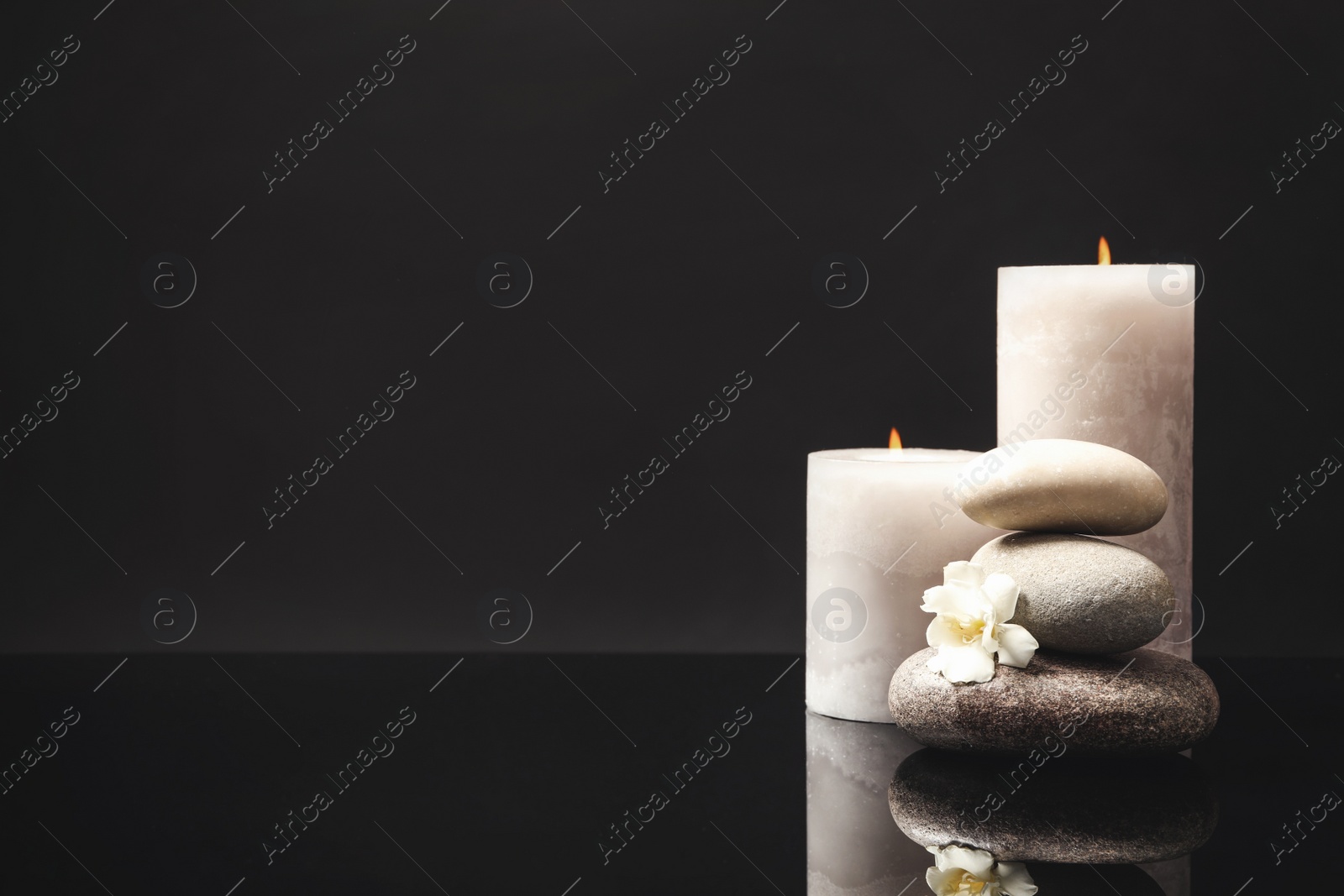 Photo of Stack of spa stones, burning candles and fresh flower on mirror surface. Space for text