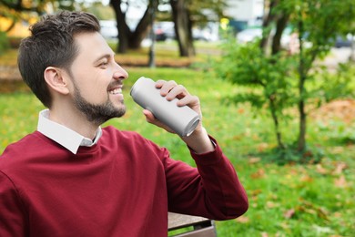 Photo of Happy man drinking from tin can in park. Space for text