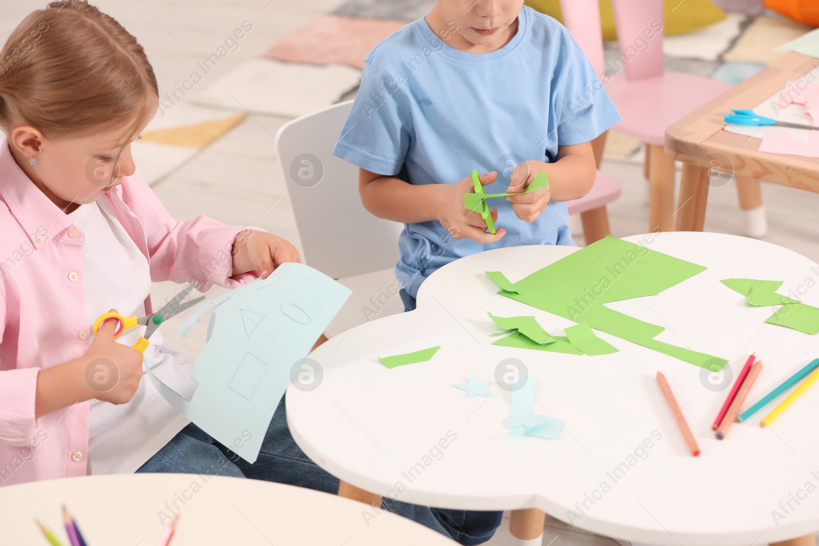 Photo of Cute little children cutting color paper with scissors at desk in kindergarten. Playtime activities