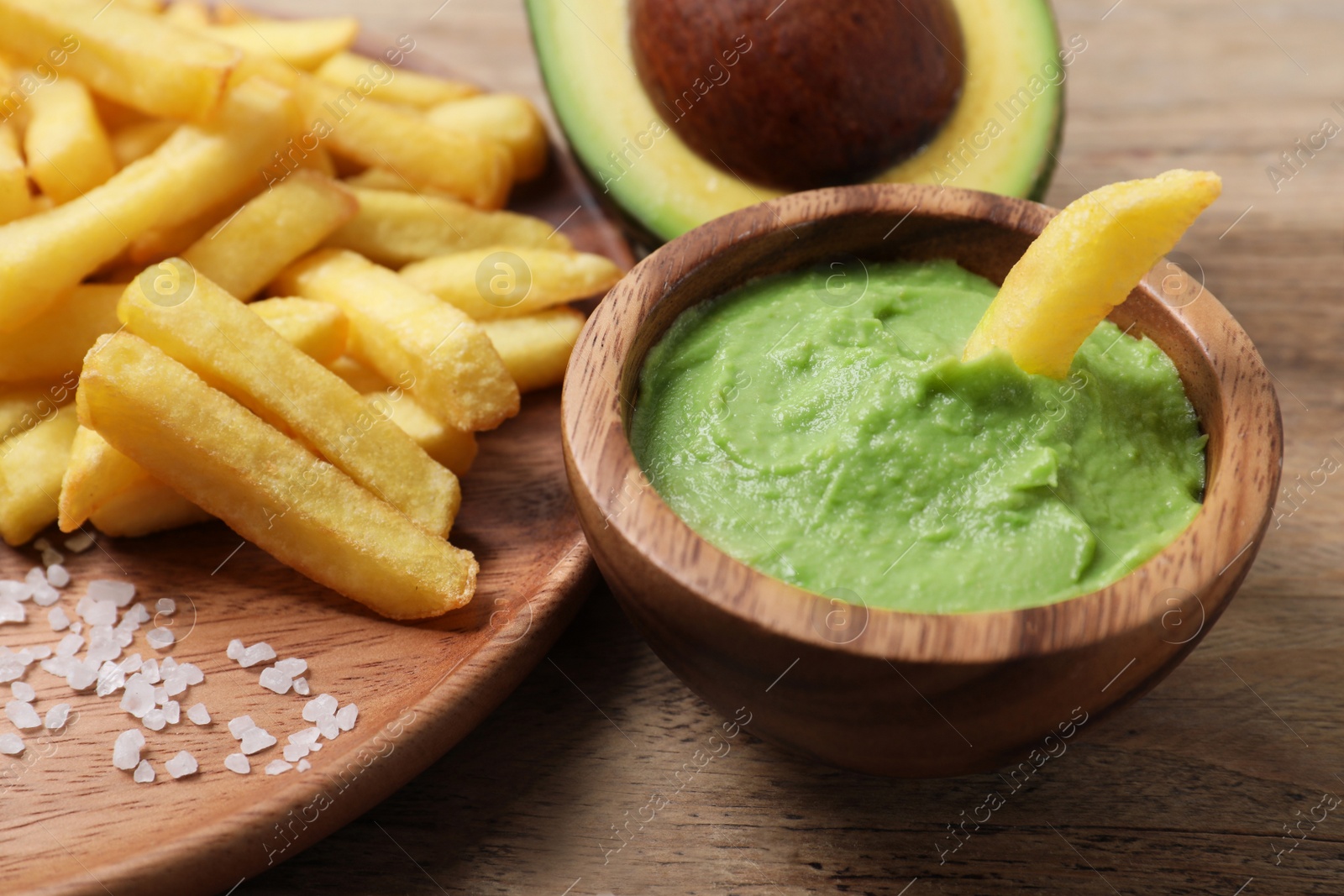 Photo of Plate with french fries, guacamole dip and avocado served on wooden table, closeup