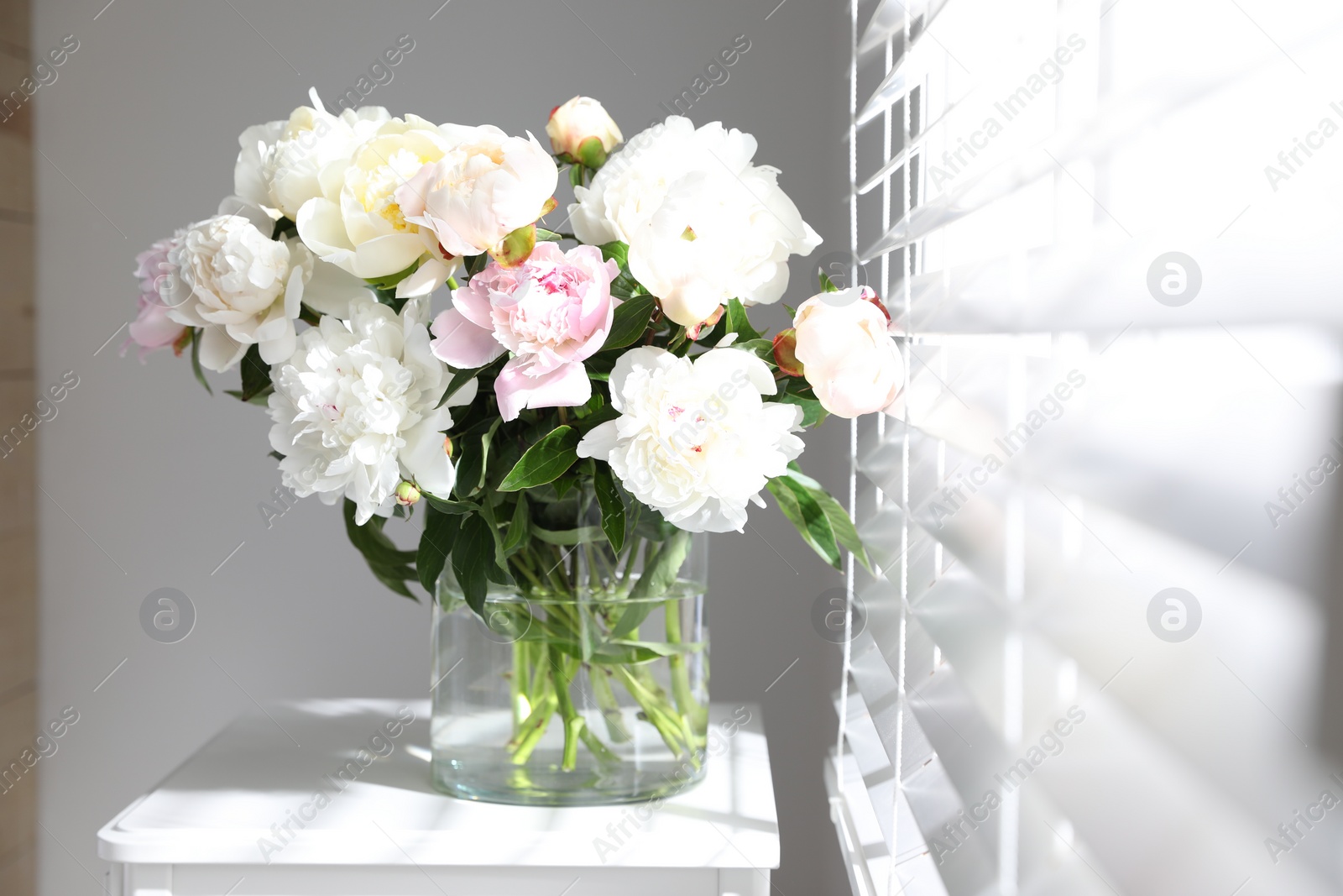 Photo of Beautiful peonies in vase on table near window indoors