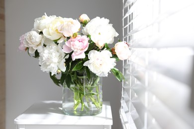 Beautiful peonies in vase on table near window indoors