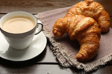 Photo of Delicious fresh croissants and cup of coffee on wooden table, closeup