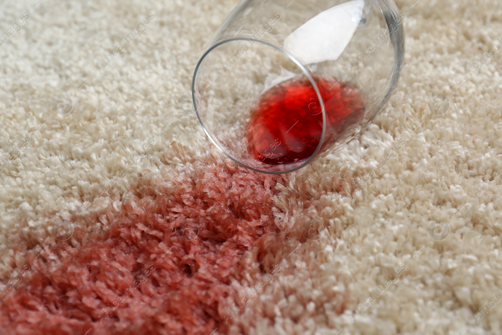 Photo of Overturned glass and spilled red wine on soft carpet, closeup