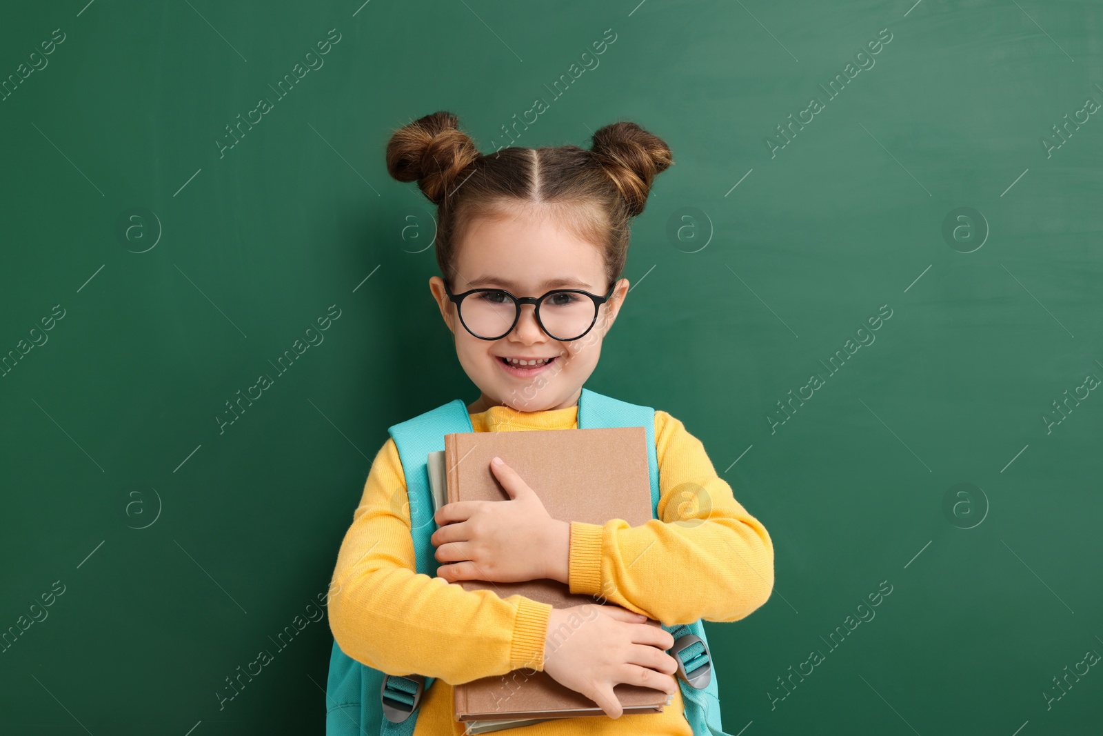 Photo of Happy little school child with notebooks near chalkboard