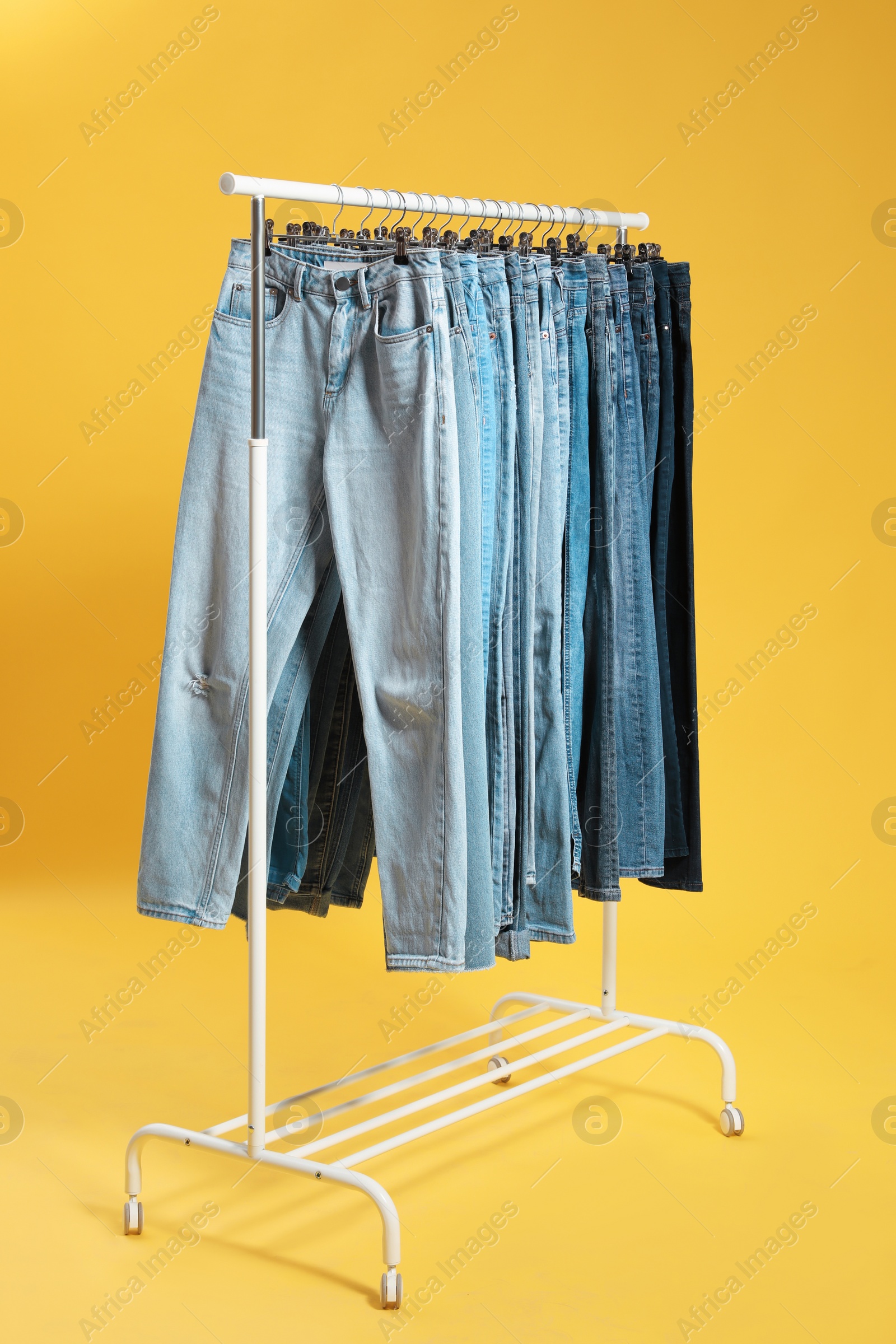 Photo of Rack with different jeans on yellow background