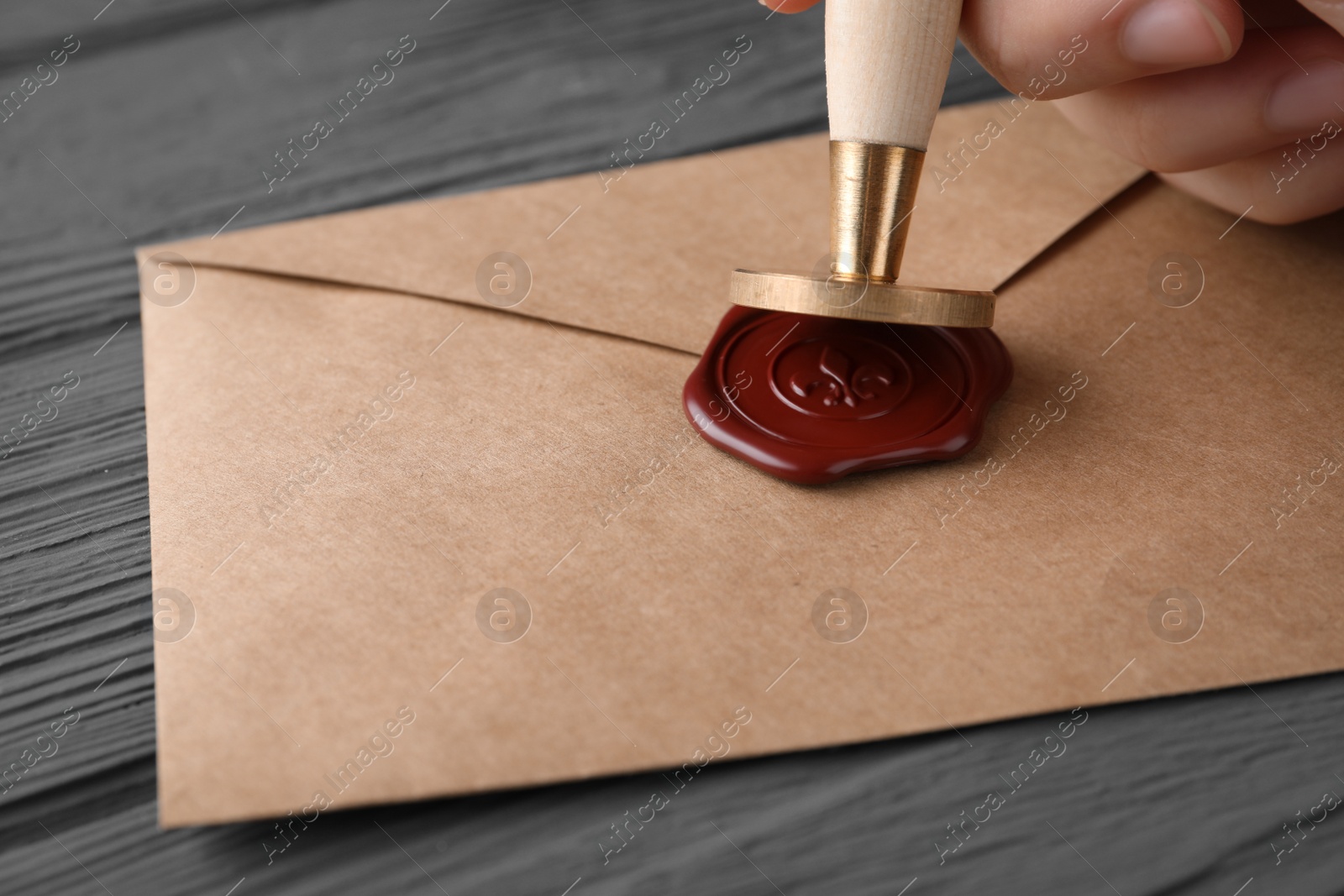 Photo of Woman sealing envelope at black wooden table, closeup