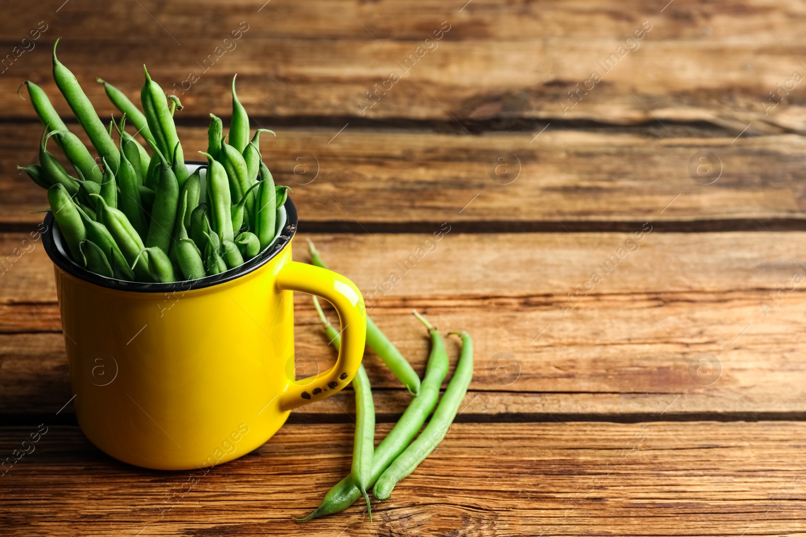 Photo of Fresh green beans in mug on wooden table, space for text