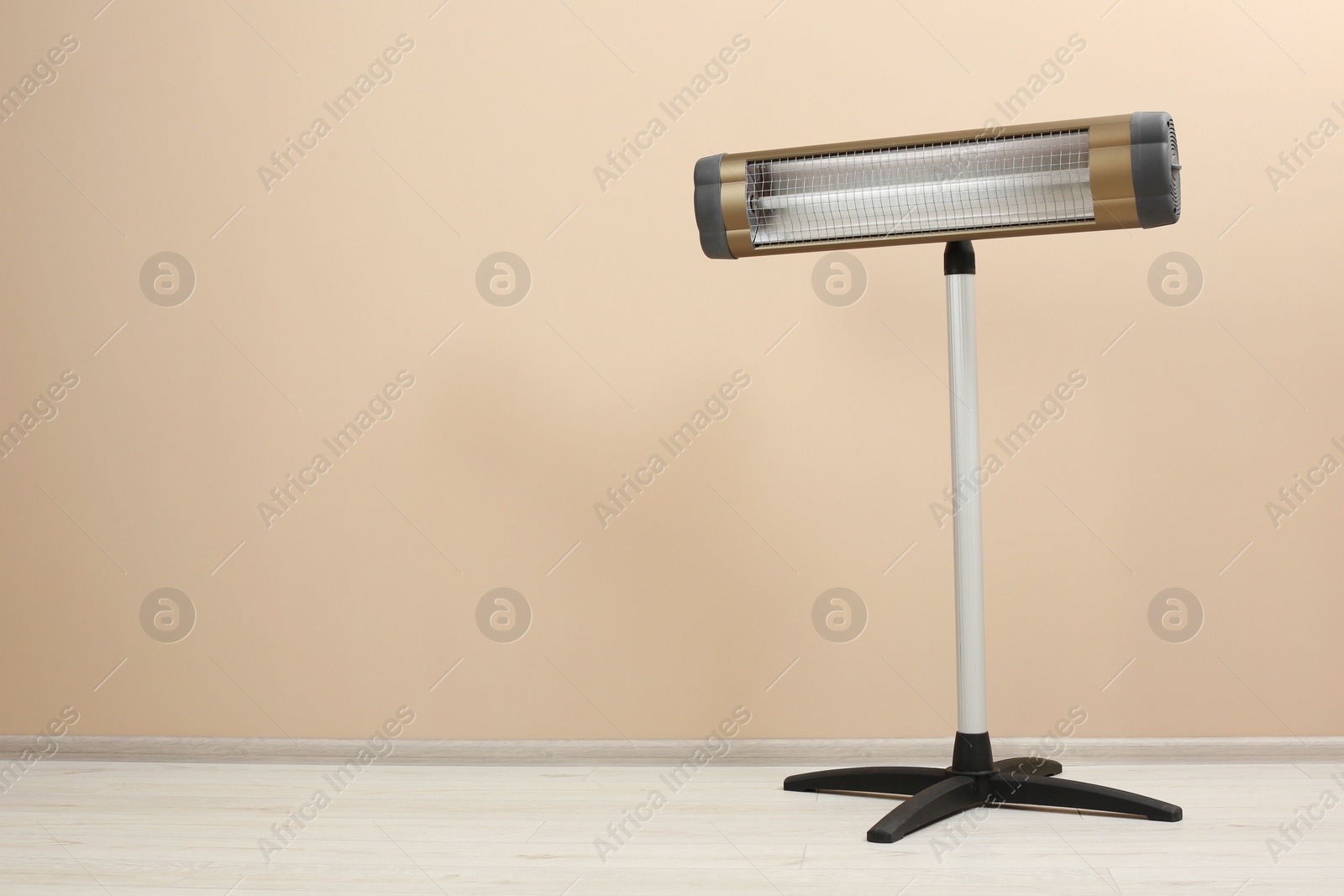 Photo of Modern electric infrared heater on floor near beige wall, space for text