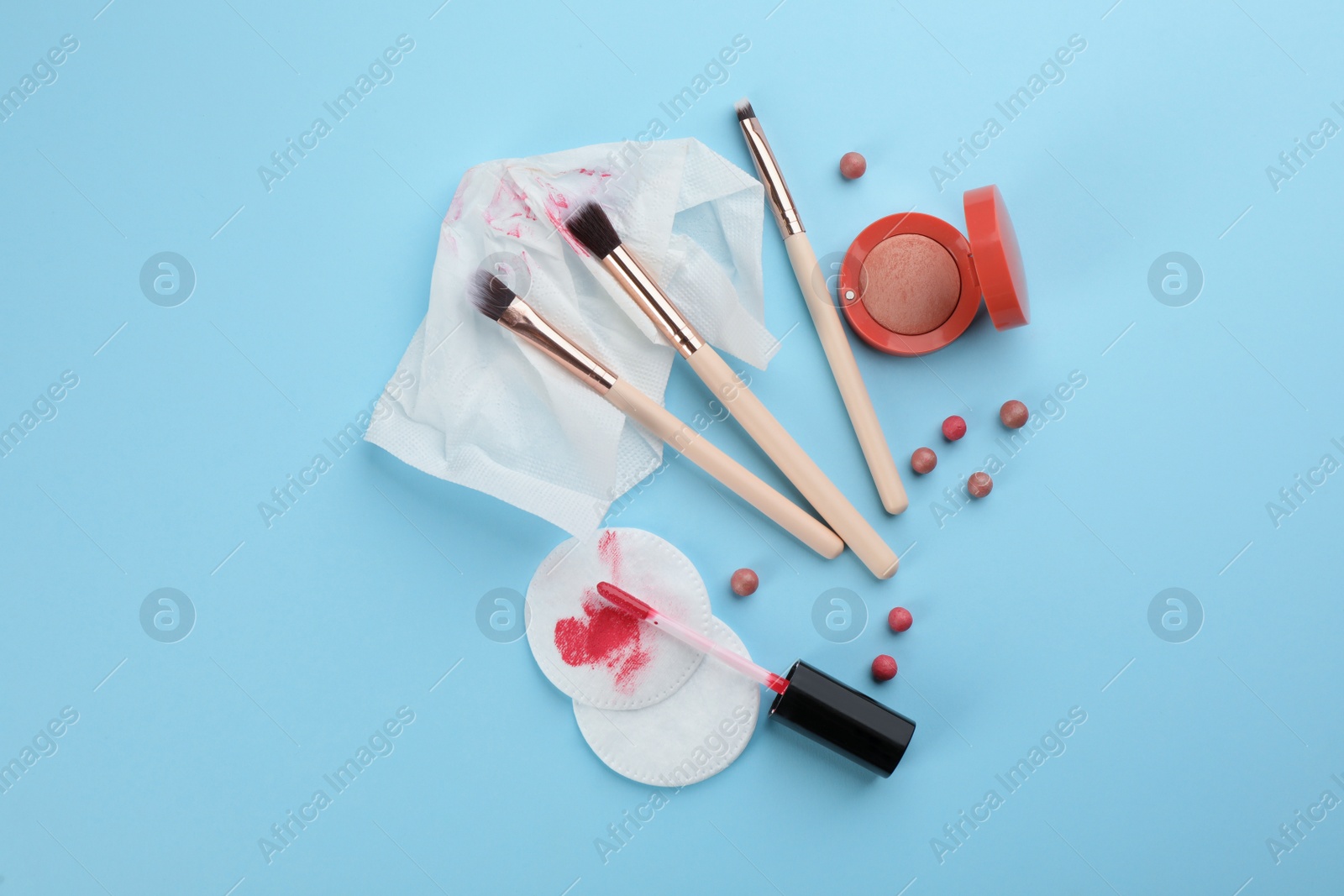 Photo of Dirty cotton pads, wet wipe and cosmetic products on light blue background, flat lay
